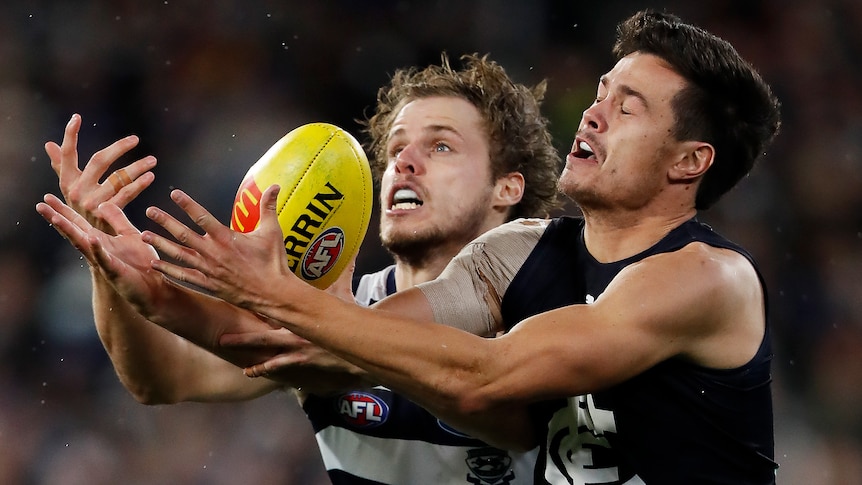 A Carlton AFL player attempts to mark the ball while being challenged by a Geelong opponent.