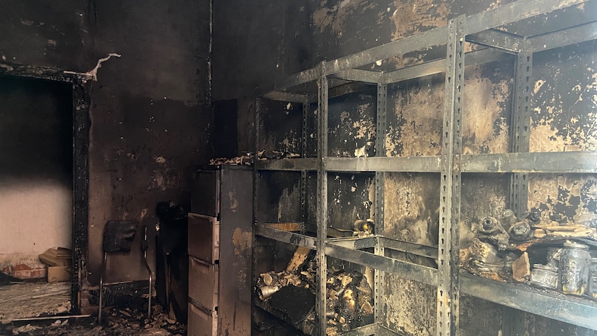 Soot covered walls of a burnt room with empty shelves, everything destroyed
