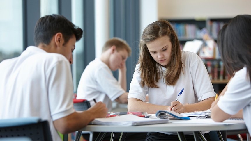 diverse high school students in white uniform writing in notebooks