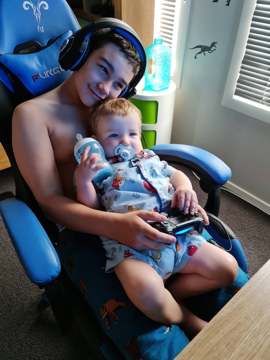 Zane Mellor cradles his younger brother while wearing gaming headphones.