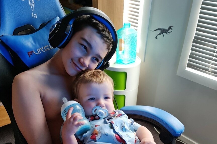 Zane Mellor cradles his younger brother while wearing gaming headphones.