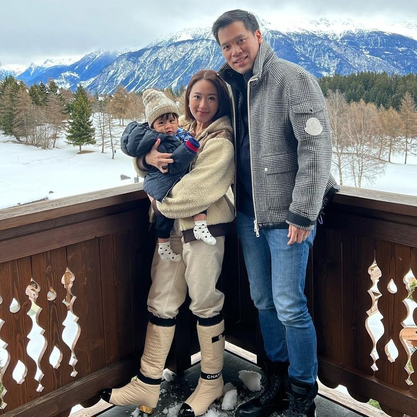 A man and a woman pose with a small child on a balcony overlooking a snowy mountain