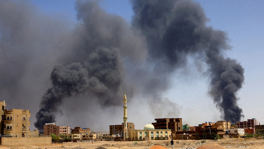  A man walks while smoke rises above buildings after aerial bombardment