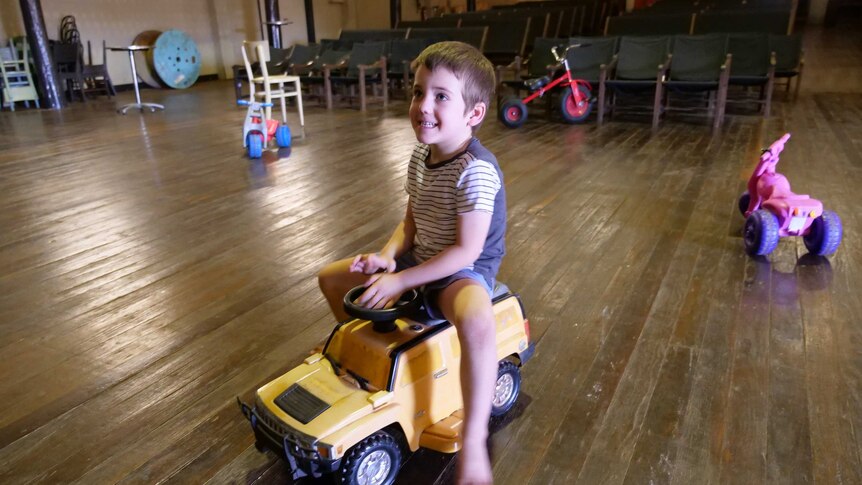 A young boy rides a plastic toy truck in the middle of an old theatre