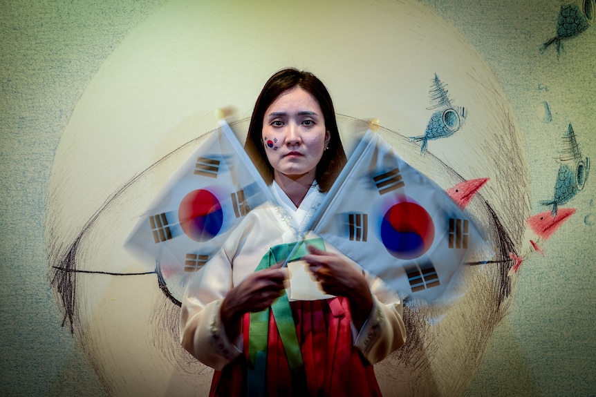 A woman looks at the camera, holding two South Korean flags which are blurred.