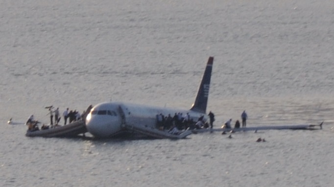 A plane in river with passengers on the wings