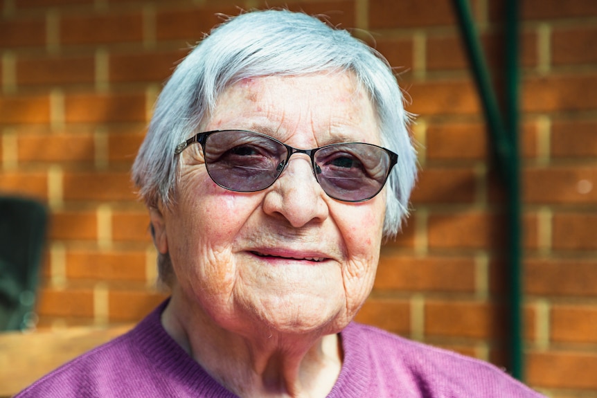 Ester Cerda, wearing tinted glasses, smiles gently in a portrait photograph.