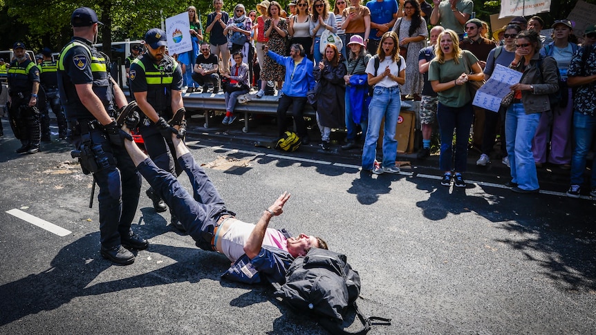 Police drag a man by the feet as he makes a peace gesture.