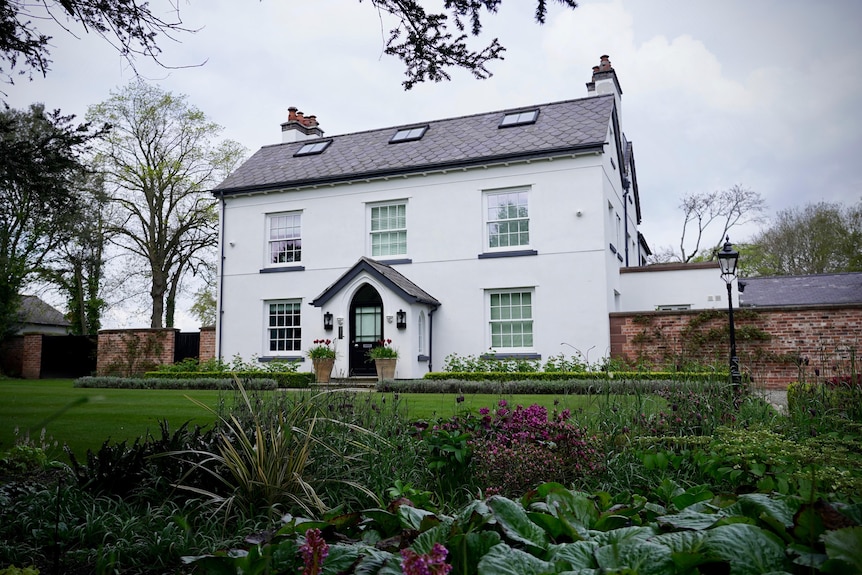 A white two-storey house with a green garden in front of it. 
