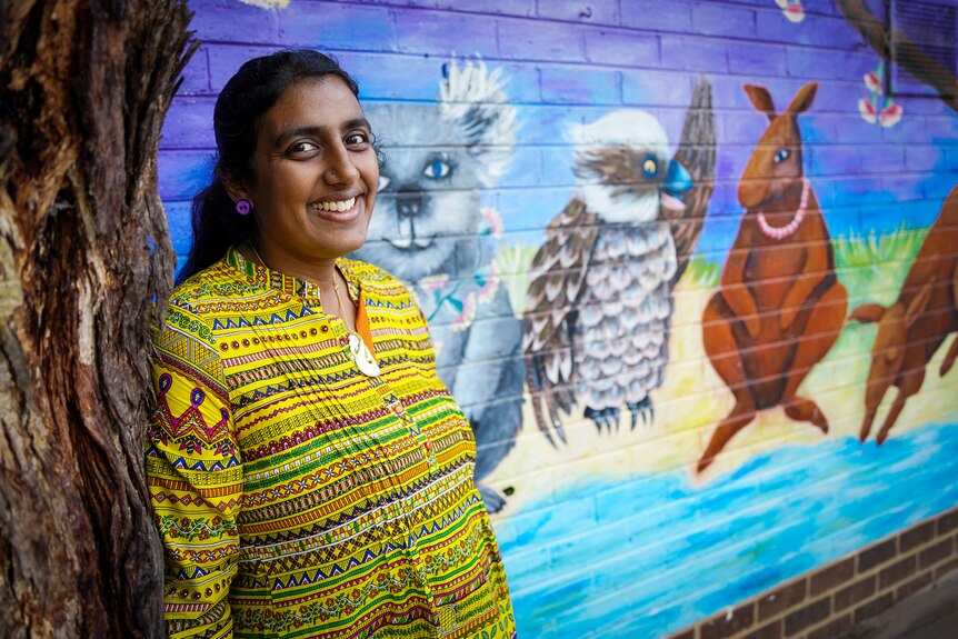 A woman in a yellow blouse poses for a portrait in front of a colourful wall