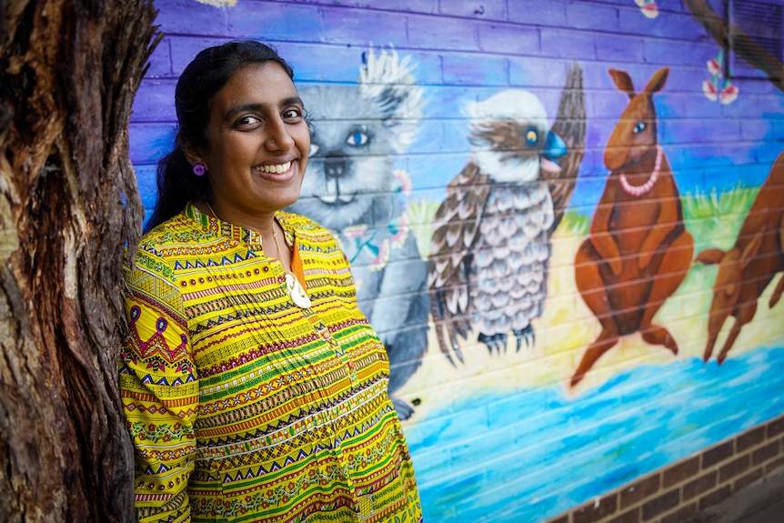 A woman in a yellow blouse poses for a portrait in front of a colourful wall