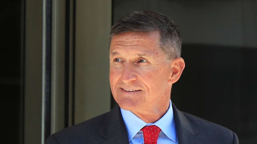 Former Trump national security adviser Michael Flynn looks to the side with a smile, wearing a suit and red tie.