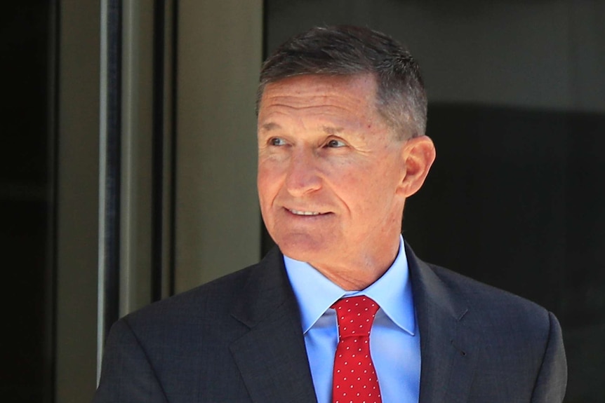 Former Trump national security adviser Michael Flynn looks to the side with a smile, wearing a suit and red tie.