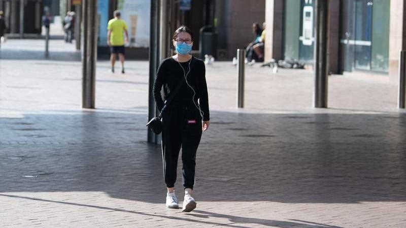 A lone woman wearing a face mask walking down the street.