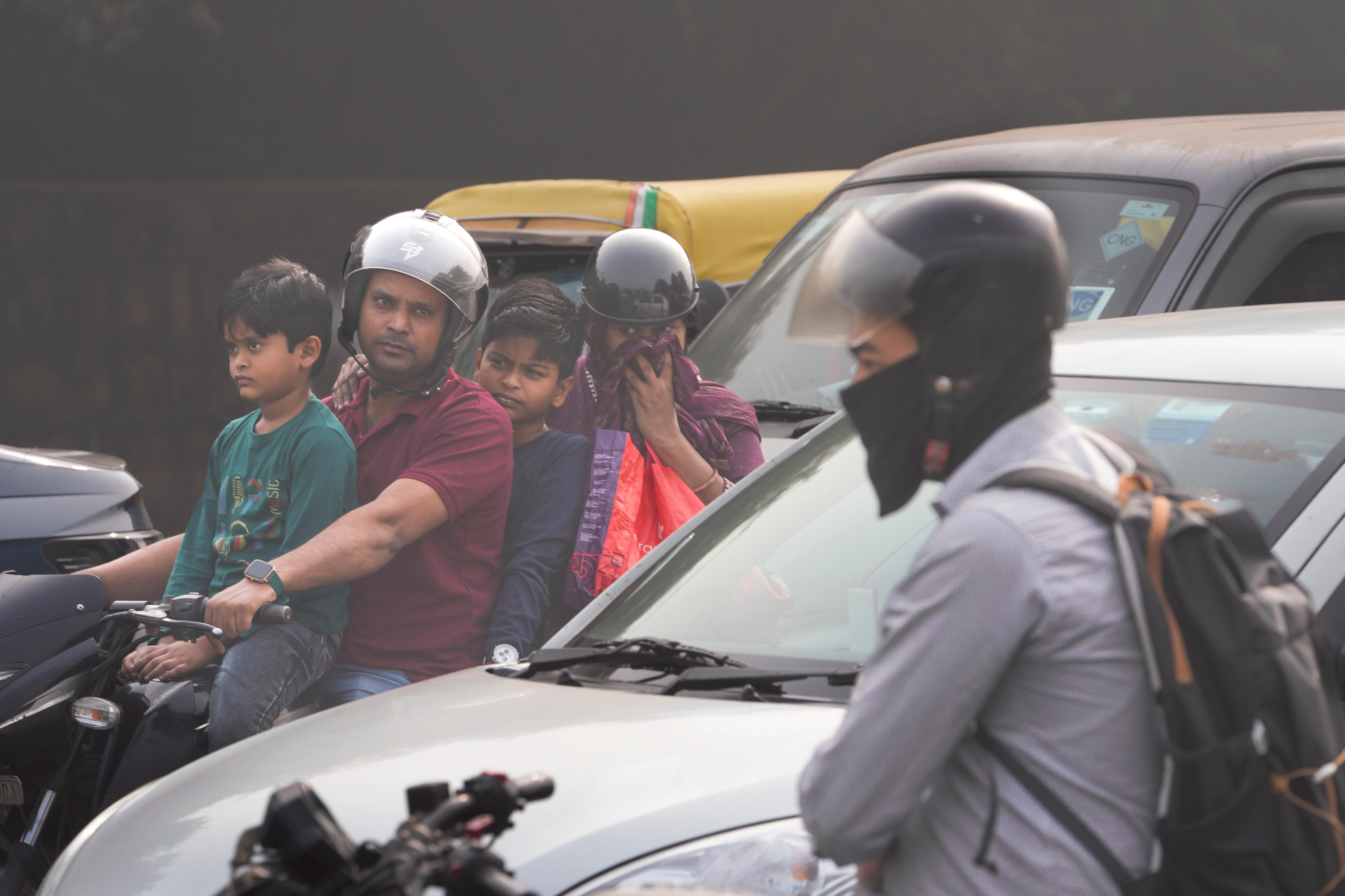 A family of four on a motorcycle waits at a traffic light surrounded by smog 