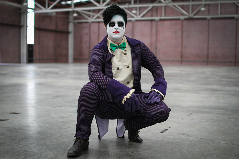 A man in a bright purple suit and green bow tie crouching down.