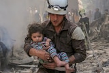 A member of Syria Civil Defence carries a child amid a ruined building