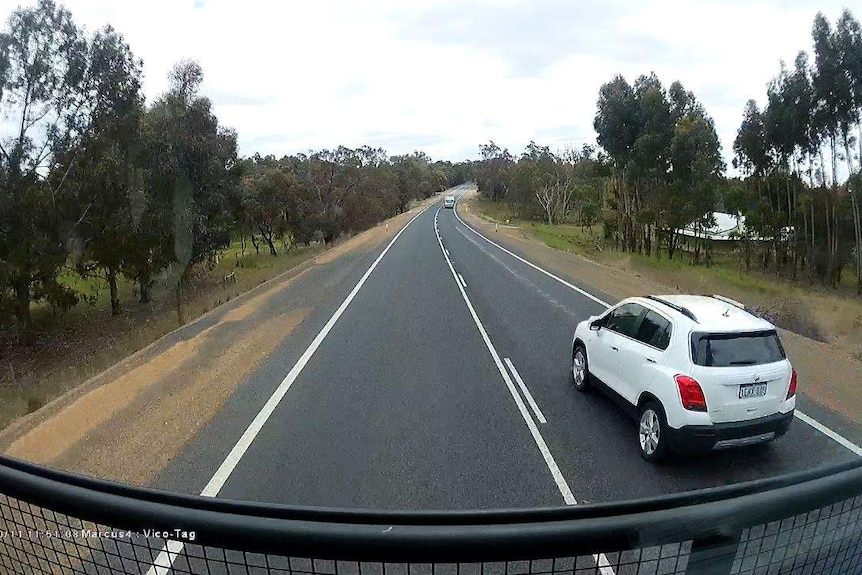A dash cam screen shot showing a car passing a truck with an oncoming truck in the distance.