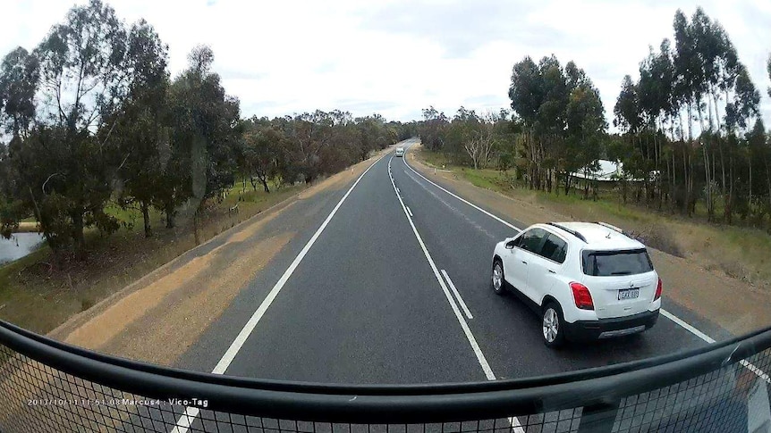 A dash cam screen shot showing a car passing a truck with an oncoming truck in the distance.