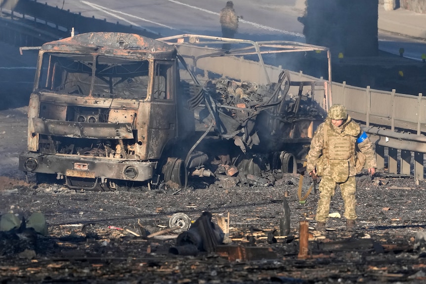 A Ukrainian soldier stands near a burning military truck.