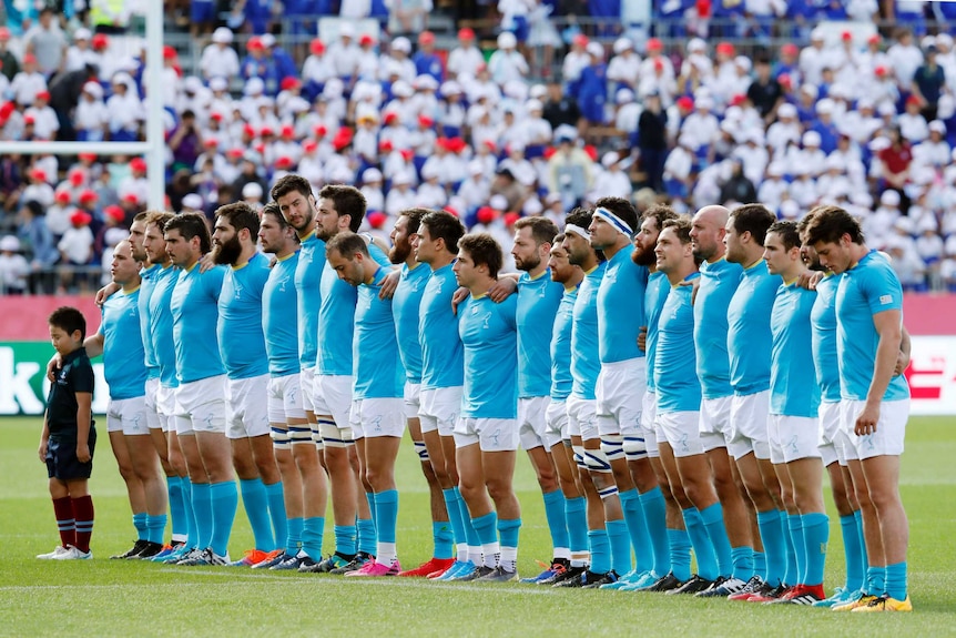 Male rugby union players stand in line alongside each other as they observe a minute's silence.