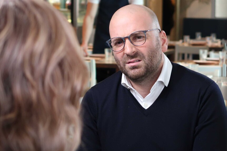 George Calombaris wears a white shirt and navy jumper
