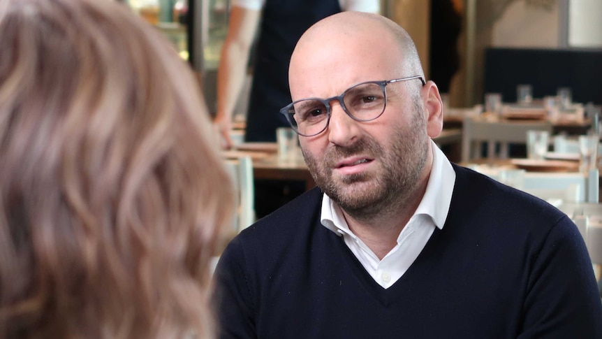 George Calombaris wears a white shirt and navy jumper