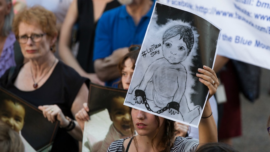 A woman holds up a poster about child asylum seekers.
