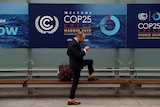 A man checking his phone with the COP25 sign in the background
