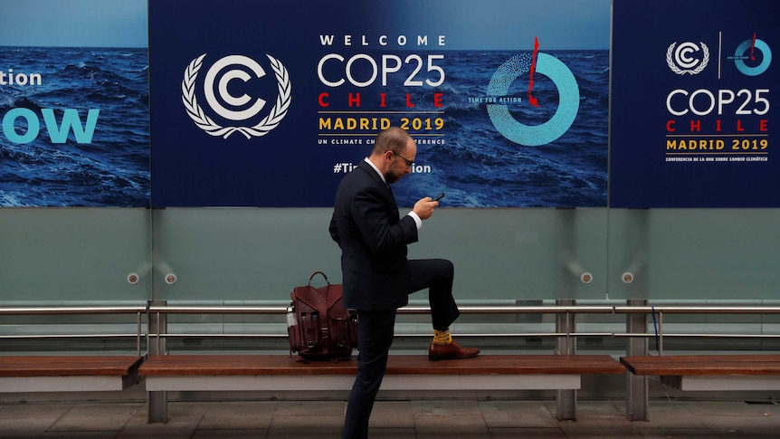 A man checking his phone with the COP25 sign in the background