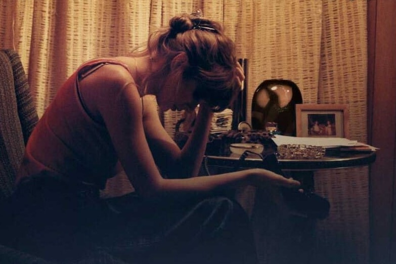 Taylor Swift sits on an armchair holding her head in her hands, a promotional image for her album Midnights