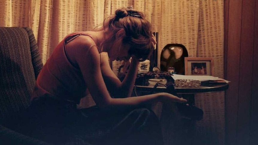Taylor Swift sits on an armchair holding her head in her hands, a promotional image for her album Midnights