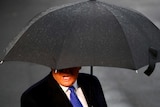 On a rainy day, Donald Trump's mouth and body are seen under a black umbrella.