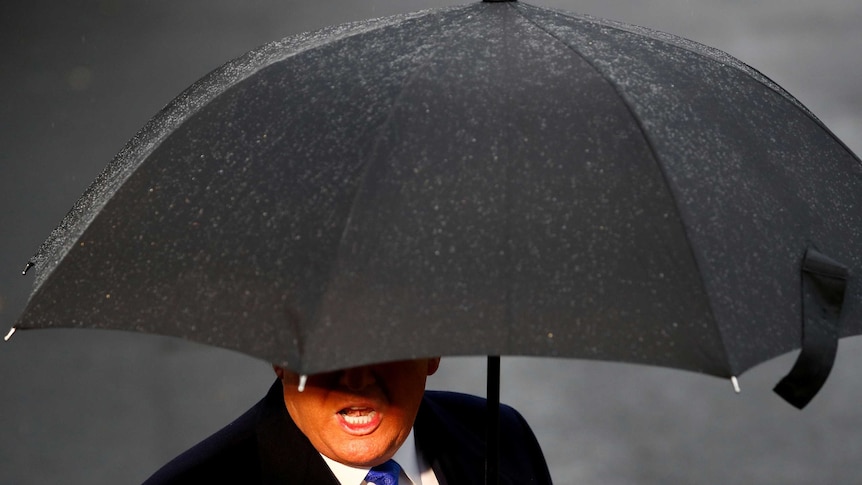 On a rainy day, Donald Trump's mouth and body are seen under a black umbrella.