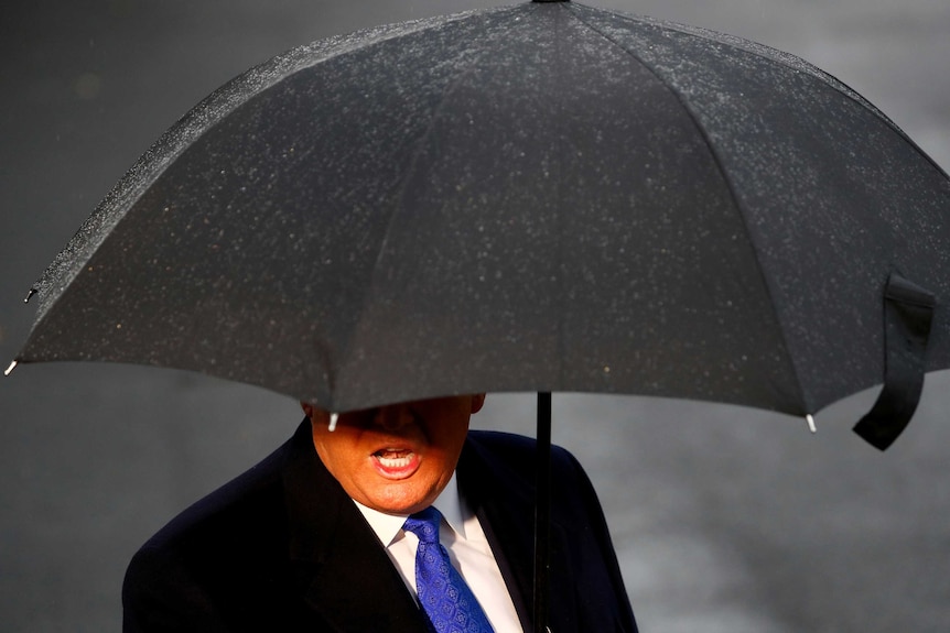 On a rainy day, Donald Trump's mouth and body are seen under a black umbrella.