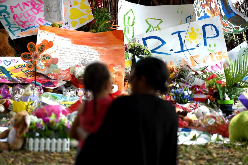 Mourners look at a floral tribute next to the Manoora home.