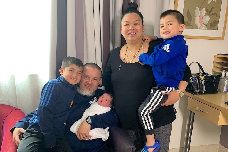 The Martinez family in a hospital room with their newborn baby girl wrapped in a white blanket.