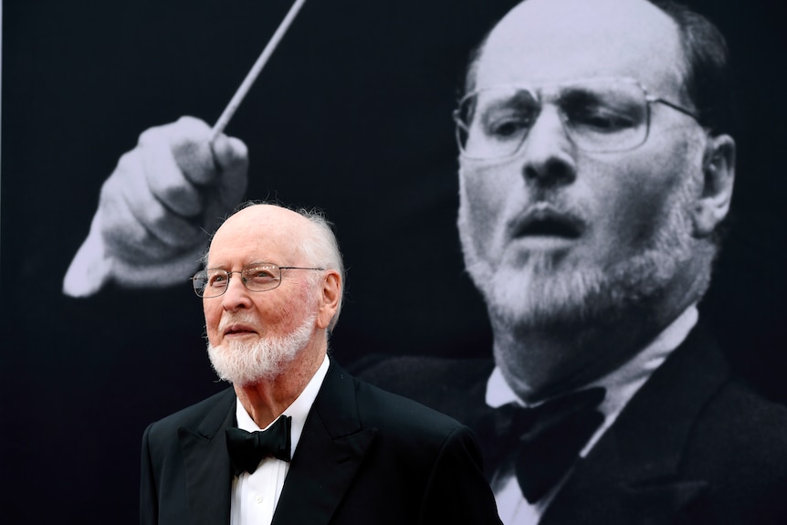 John Williams stands in front of a projected black and white image of himself.