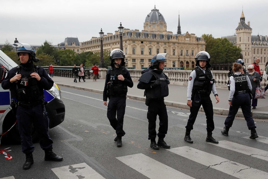 Heavily armed police officers stand outside an historic building.