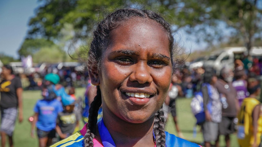 An Indigenous teenager girl with her hair in plaits smiles to the camera.