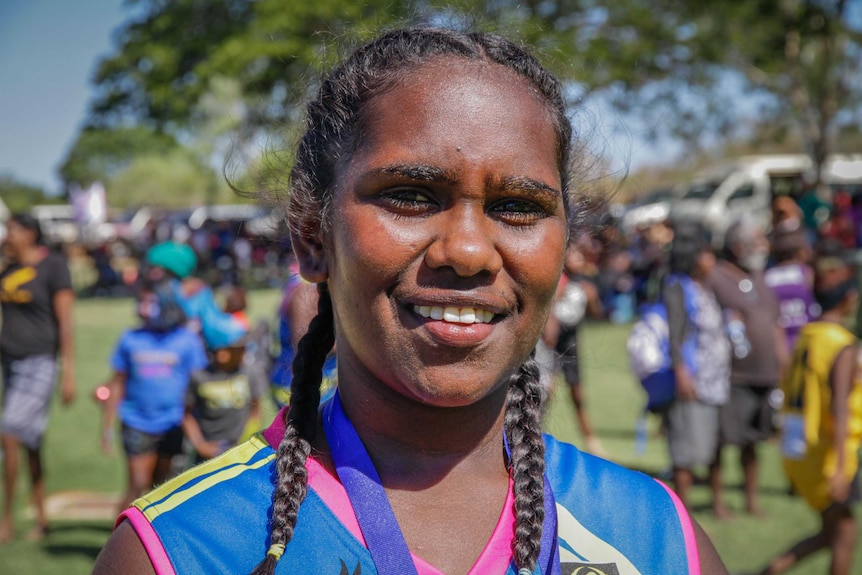 An Indigenous teenager girl with her hair in plaits smiles to the camera.
