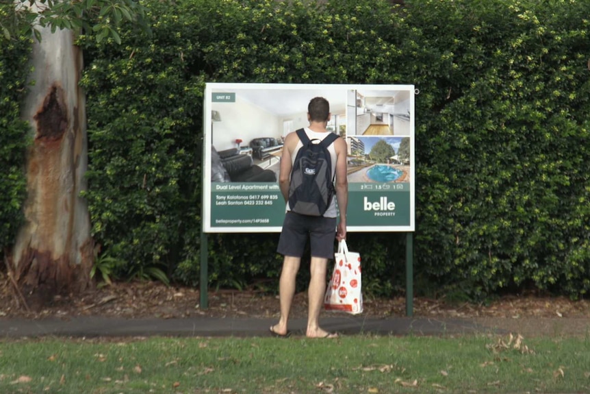 Man looking at for sale sign for apartment