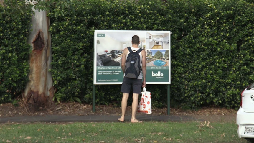 Man looking at for sale sign for apartment