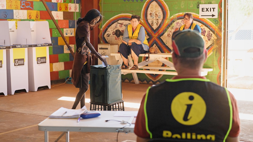 A woman places a vote in a ballot box as a polling official watches on.
