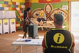 A woman places a vote in a ballot box as a polling official watches on.