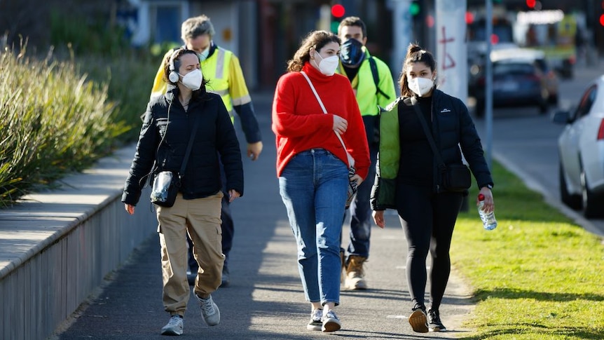 Three young women in masks walk on a Melbourne street. Two men wearing high-vis clothing and masks walk behind them.