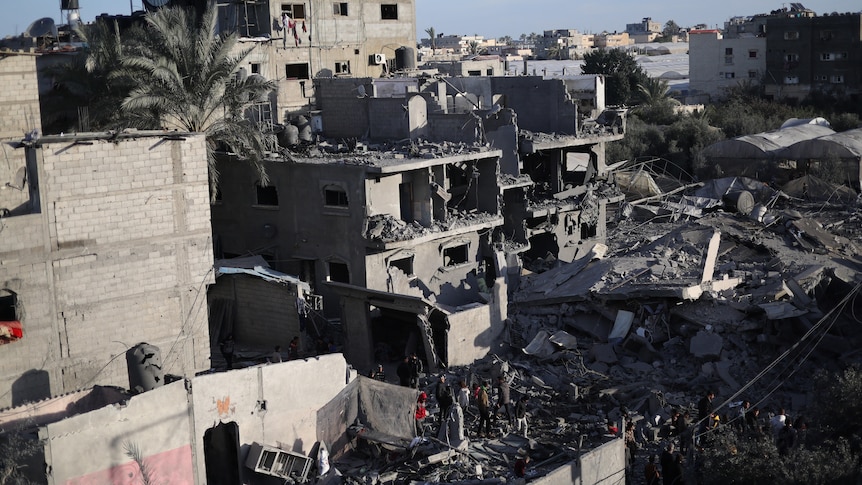 A damaged building in Rafah, rubble and debri being combed thorgh by people