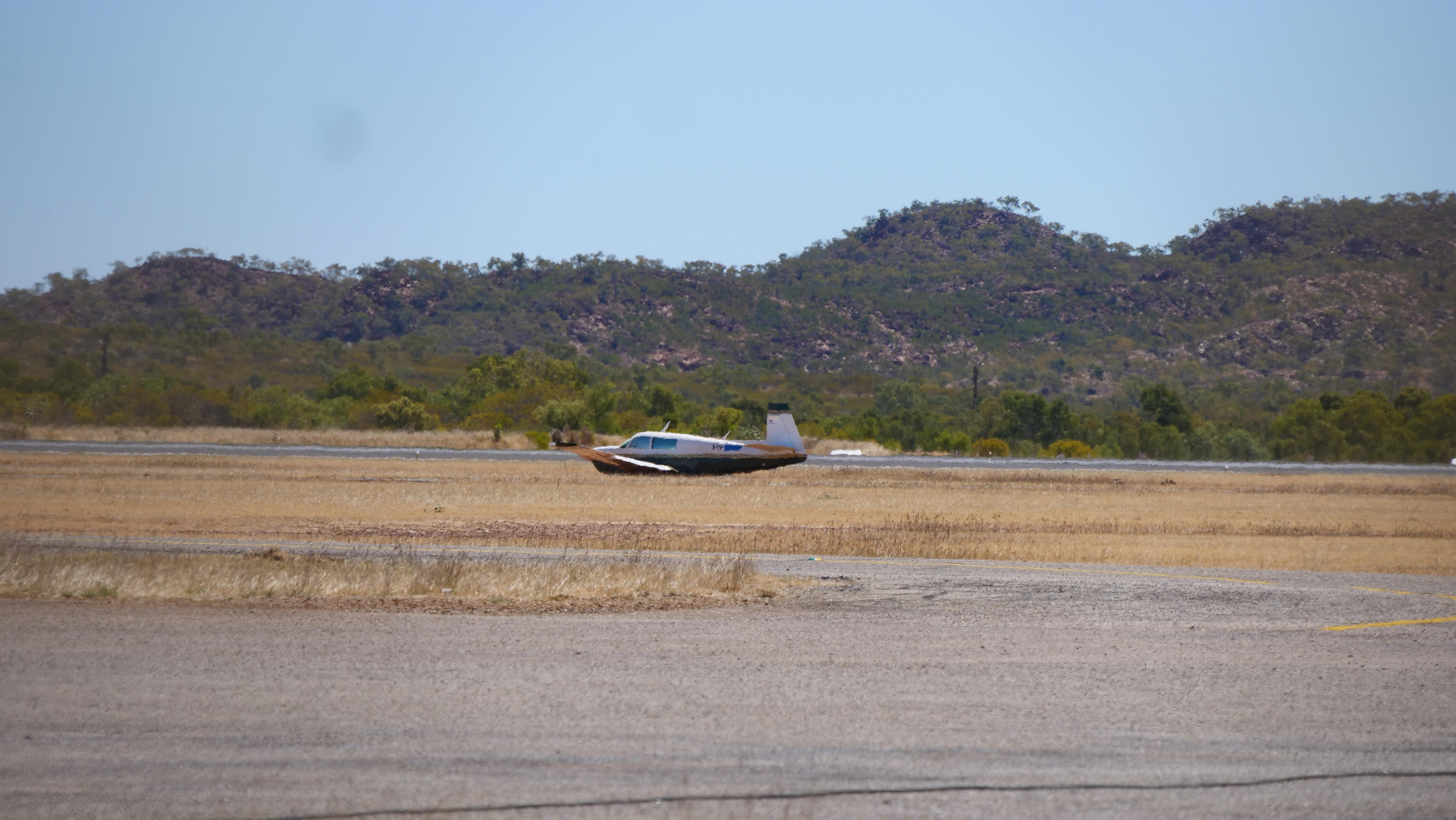a light aircraft on a field next to an airstrip without its landing gear