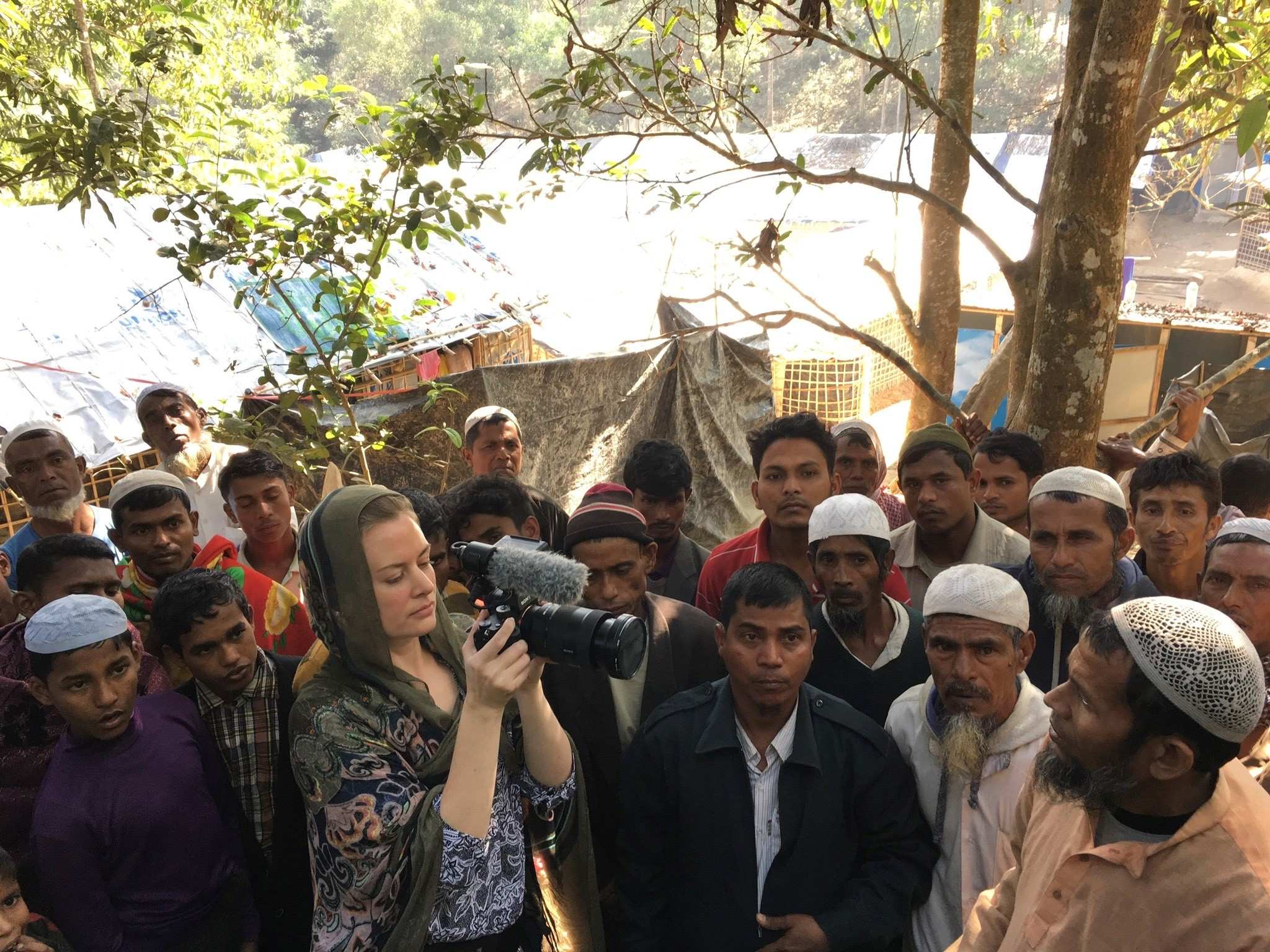 Heanue wearing headscarf filming men in refugee camp.