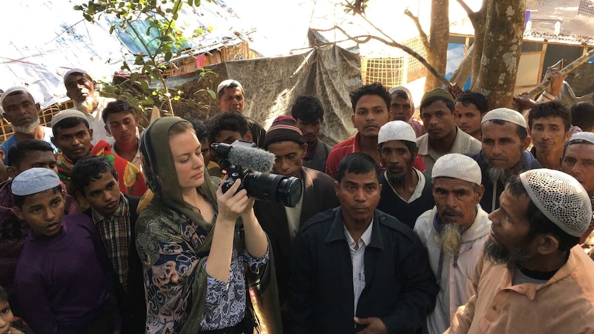 Heanue wearing headscarf filming men in refugee camp.